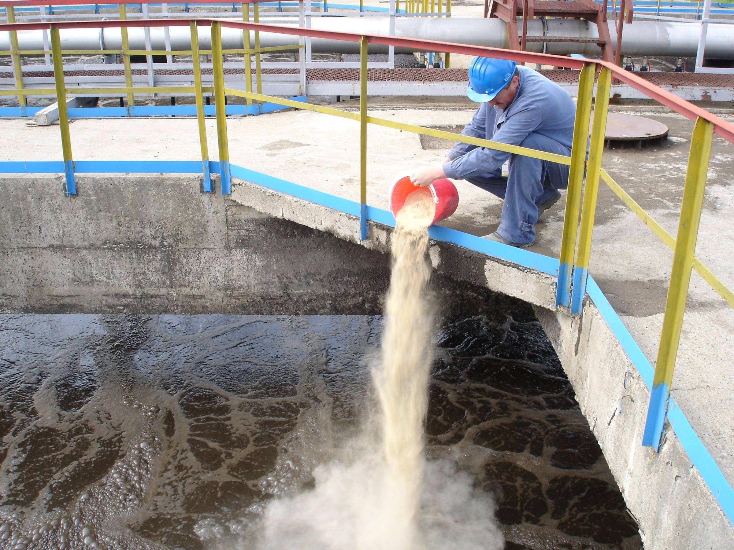 Operator care aplică produsul sub formă de pudră într-un bazin al stației de epurare