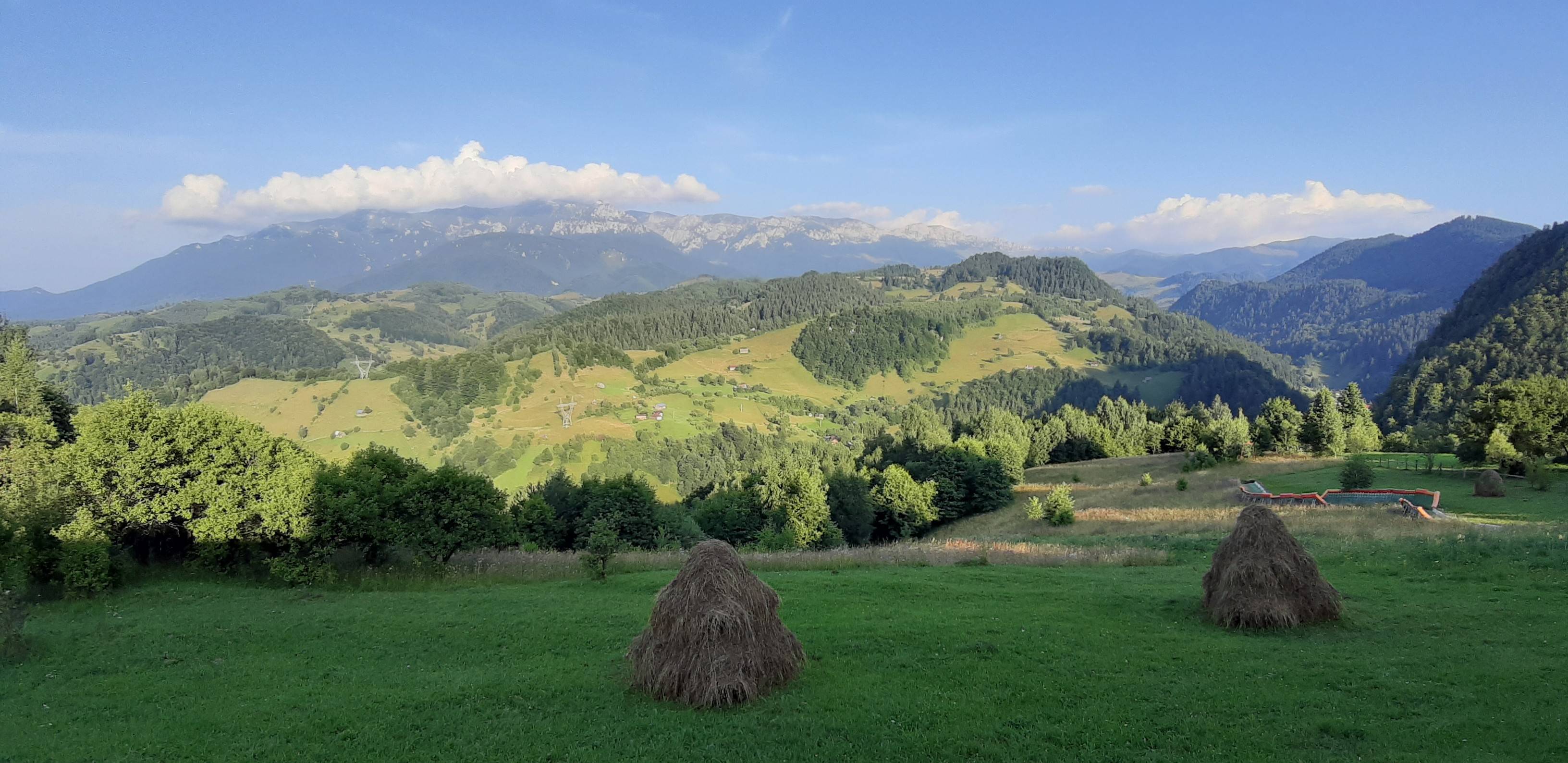 Peisaj montan cu fânețe și căpițe de fân